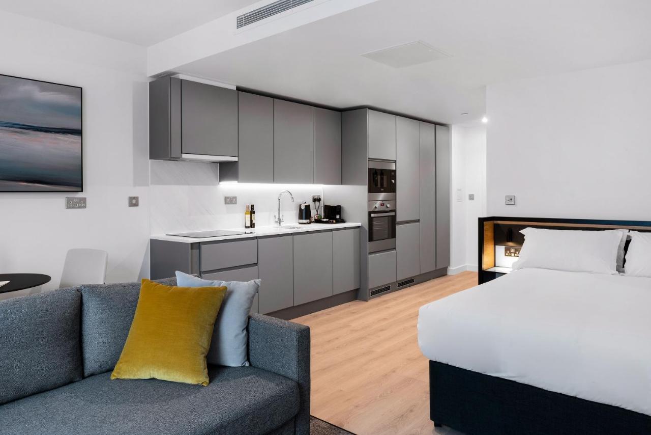 Citysuites 2 Aparthotel Manchester Exteriör bild The photo shows a modern studio apartment featuring an open-plan layout. On one side, there is a kitchenette with sleek, gray cabinets and appliances, including a coffee maker and oven. Adjacent to the kitchenette is a small dining area with a table 