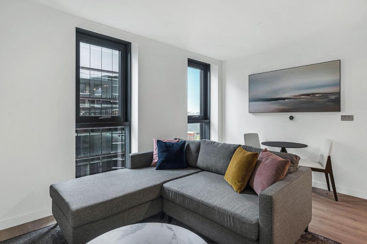 Citysuites 2 Aparthotel Manchester Exteriör bild The photo shows a modern living space featuring a gray sectional sofa adorned with colorful throw pillows. There are large windows allowing natural light to fill the room, offering a view of the outdoors. A wall-mounted television is positioned above
