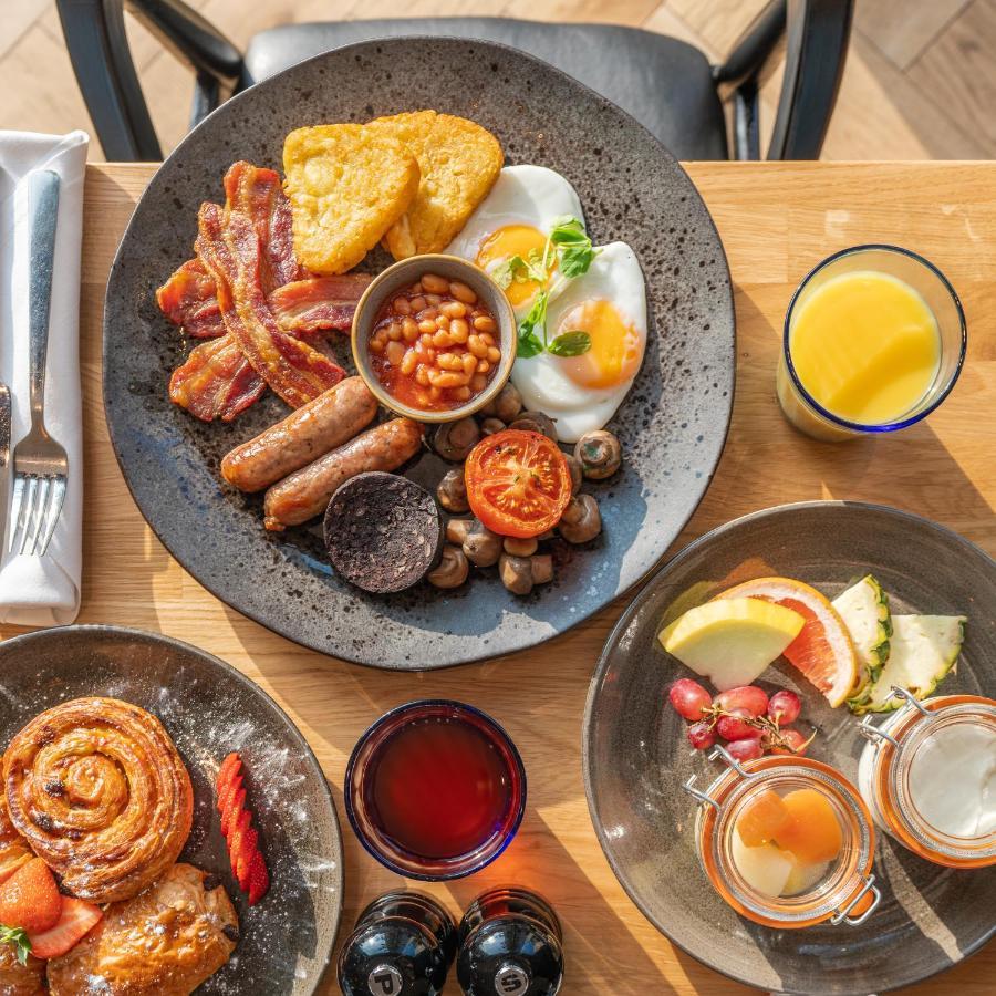 Citysuites 2 Aparthotel Manchester Exteriör bild The photo showcases a delicious breakfast spread. On a large, dark plate, there are items including crispy bacon, two fried eggs, baked beans, a grilled tomato, sautéed mushrooms, sausage links, and slices of black pudding. There's also a few pieces 