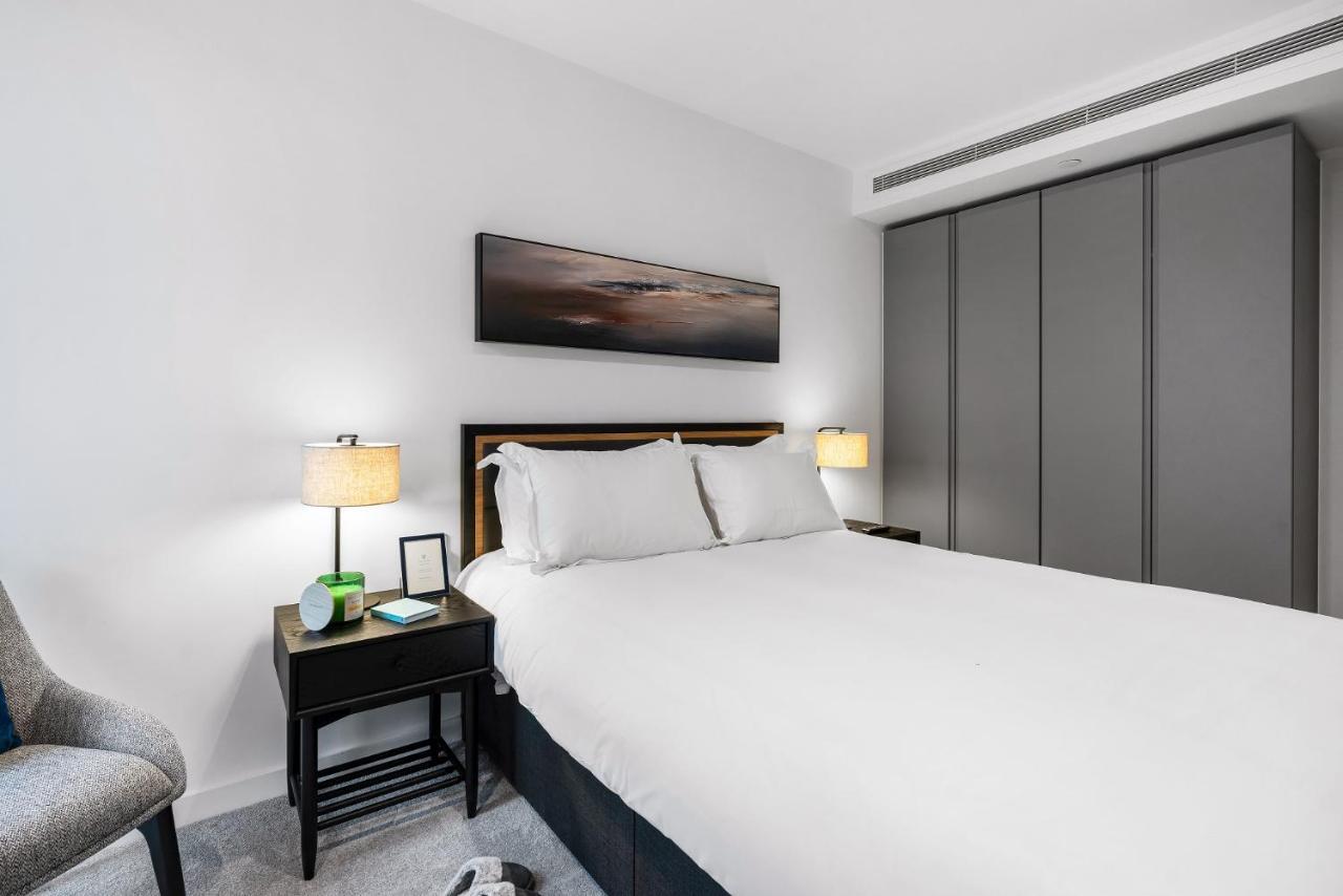 Citysuites 2 Aparthotel Manchester Exteriör bild The photo shows a modern bedroom with a neatly made bed featuring white linens and pillows. Flanking the bed are two bedside tables, each with a lamp providing soft lighting. There is a piece of artwork above the bed, which appears to depict a landsc