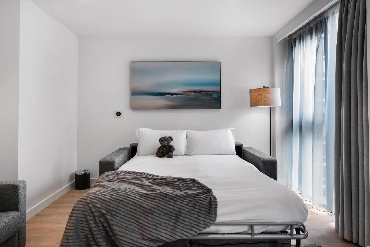 Citysuites 2 Aparthotel Manchester Exteriör bild The photo shows a modern bedroom featuring a bed with white bedding and a decorative throw blanket. There is a teddy bear placed on the bed. A piece of abstract art is hanging on the wall above the bed. The room has a large window with sheer curtains
