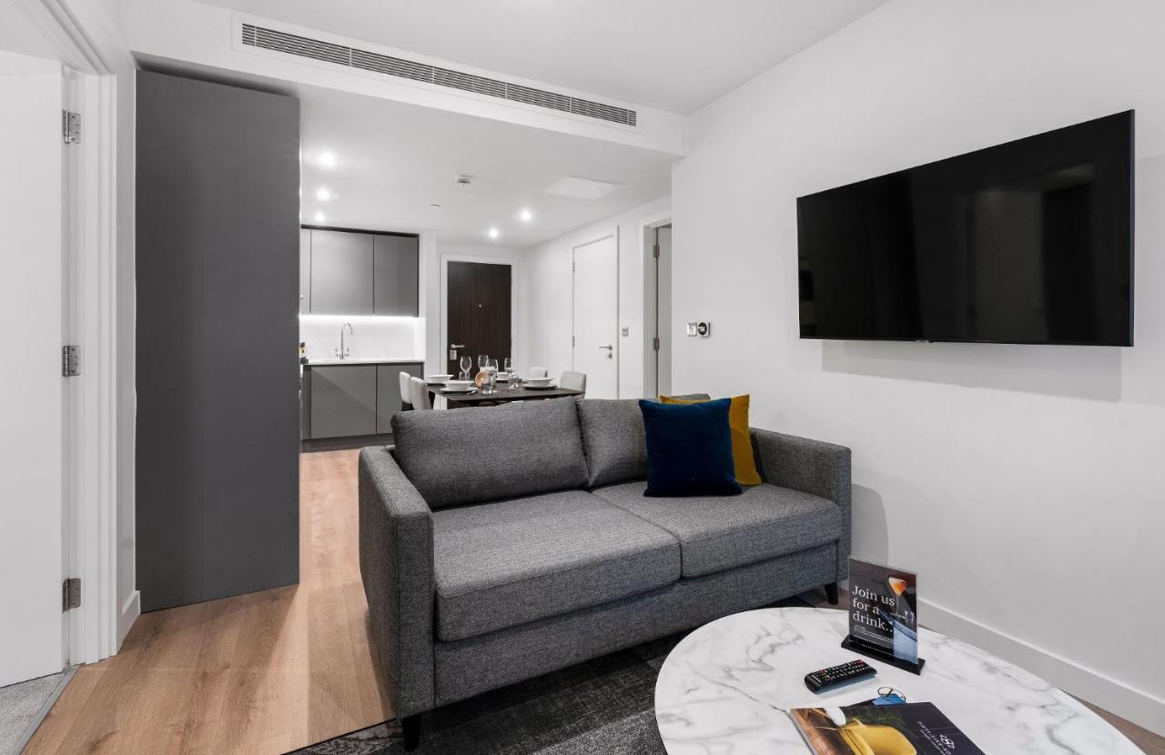 Citysuites 2 Aparthotel Manchester Exteriör bild The photo shows a modern living space that includes a gray sofa with colorful cushions, a round marble coffee table, and a flat-screen TV mounted on the wall. In the background, there is a kitchen area featuring sleek cabinets. The flooring is light 