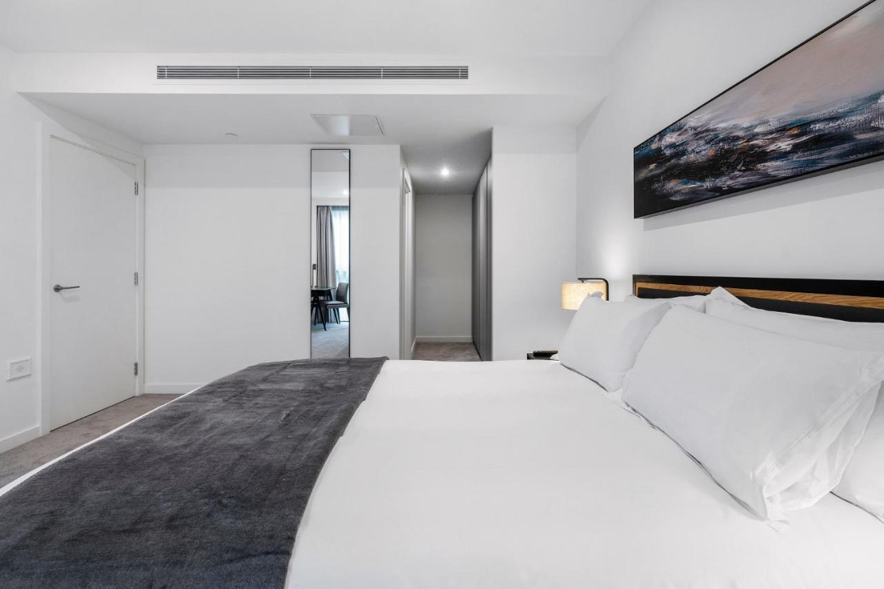 Citysuites 2 Aparthotel Manchester Exteriör bild The photo shows a modern bedroom with a minimalistic design. In the foreground, there is a neatly made bed with white linens and a dark gray throw blanket. To the side, there is a bedside lamp and a piece of abstract artwork on the wall above the bed