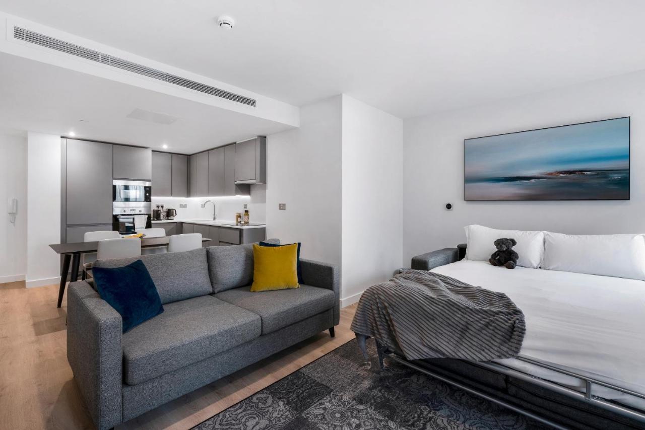 Citysuites 2 Aparthotel Manchester Exteriör bild The photo shows a modern, open-concept living space that includes a kitchen and a sleeping area. 

- **Living Area**: On the left, there's a gray sofa with a blue and yellow throw pillow. A blanket is draped over one side, and there's a small dark ru