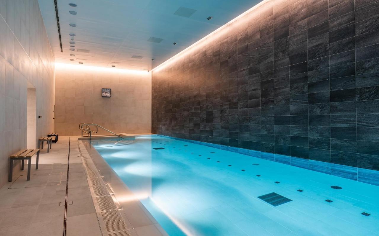 Citysuites 2 Aparthotel Manchester Exteriör bild The photo shows an indoor swimming pool area. The pool is illuminated with a soft blue light, creating a calming atmosphere. The walls are designed with dark tiles, and there is a lighter tiled area surrounding the pool. Ambient lighting is installed