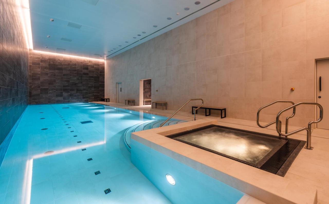 Citysuites 2 Aparthotel Manchester Exteriör bild The photo shows an indoor swimming pool area. The pool is a bright blue color and features smooth, tiled surfaces. On one side, there is a hot tub area with steps leading into it. The walls are made of light-colored stone, and there is ambient lighti