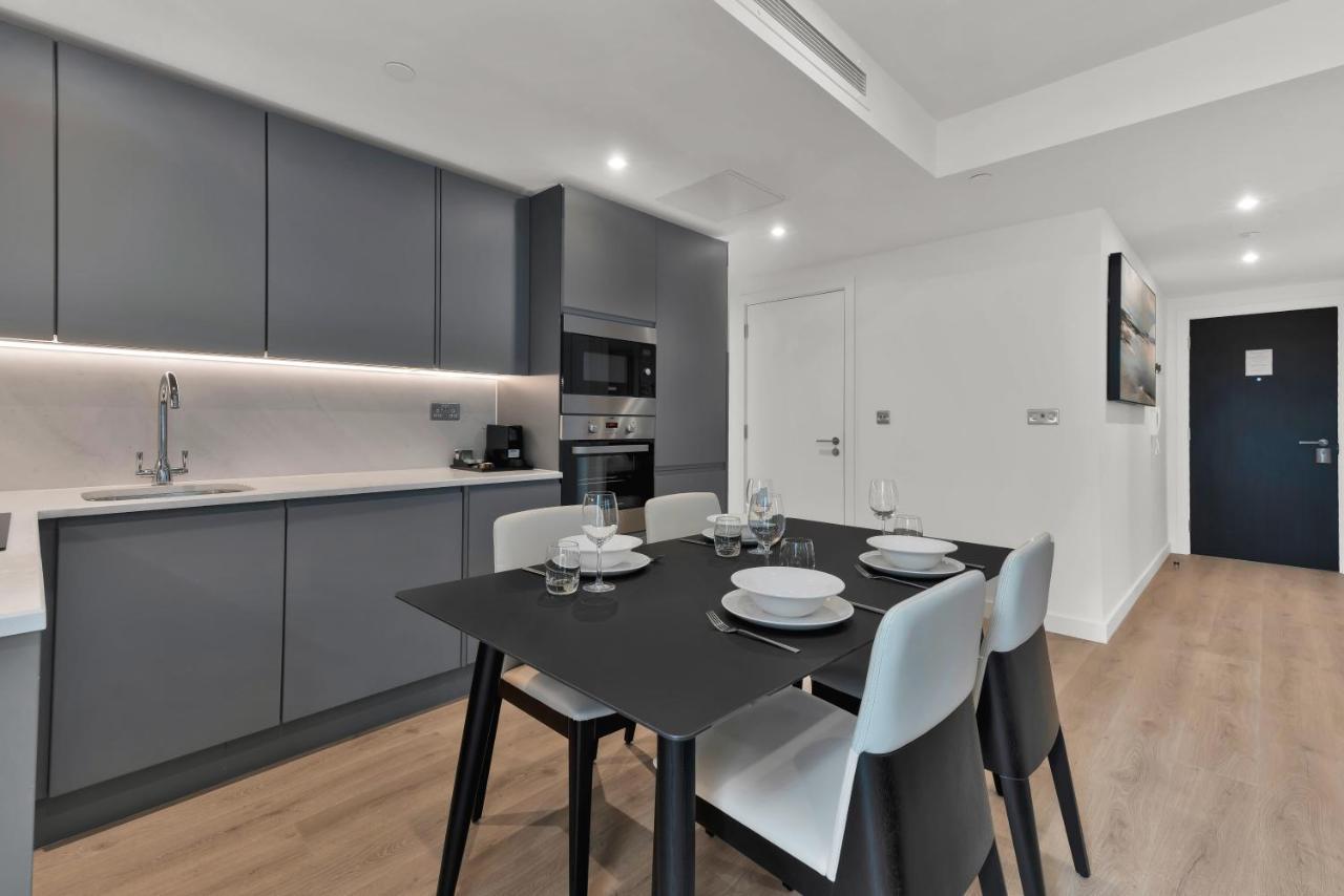 Citysuites 2 Aparthotel Manchester Exteriör bild The photo shows a modern kitchen and dining area. There are sleek gray cabinetry and countertops, with a built-in oven and microwave. The kitchen is well-lit, featuring under-cabinet lighting that adds to the contemporary feel. In the dining area, th