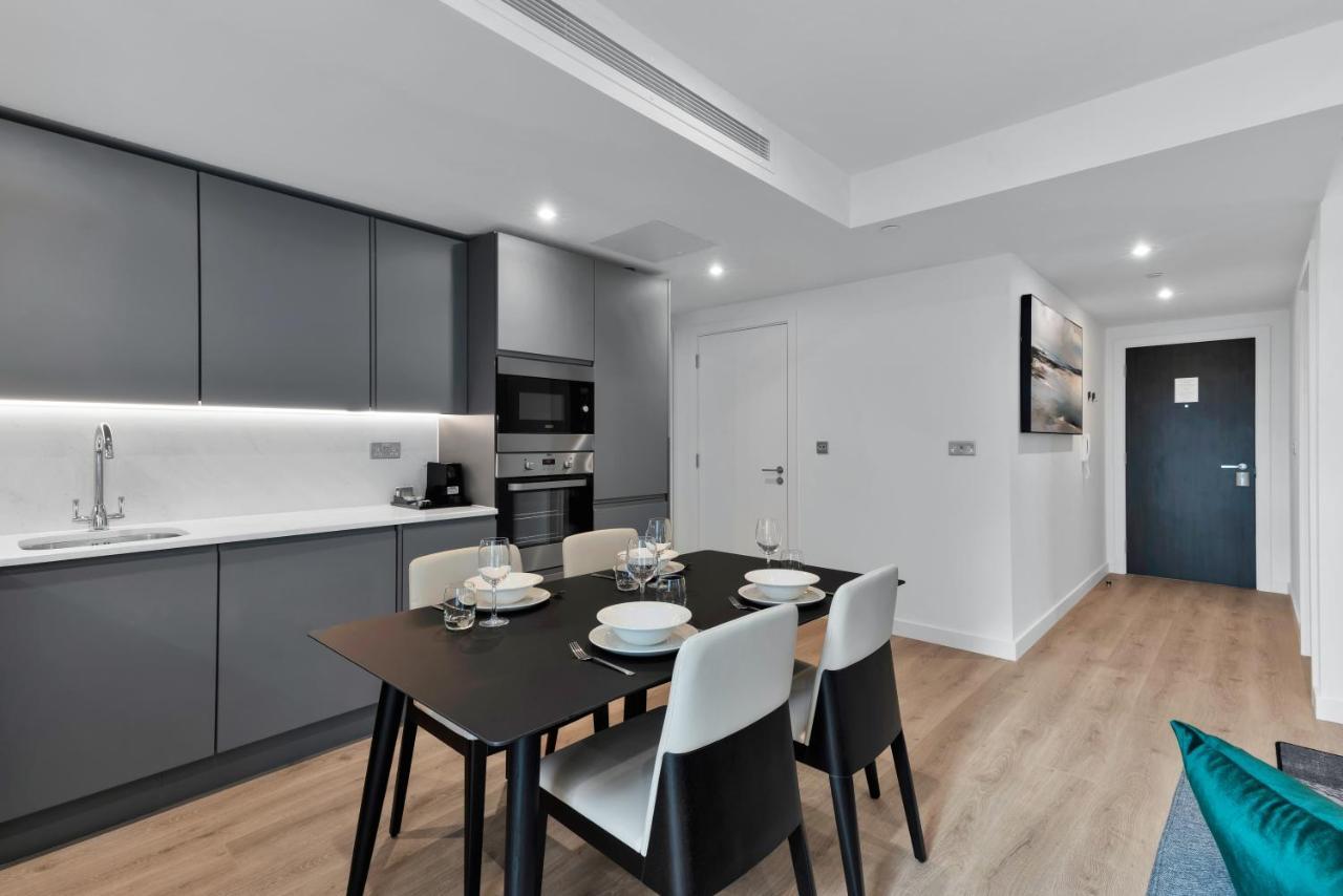 Citysuites 2 Aparthotel Manchester Exteriör bild The image shows a modern kitchen and dining area. The kitchen features sleek gray cabinets with a white countertop, and it is equipped with appliances such as a microwave. There’s a dining table set for four, with white plates and glasses ready. The 
