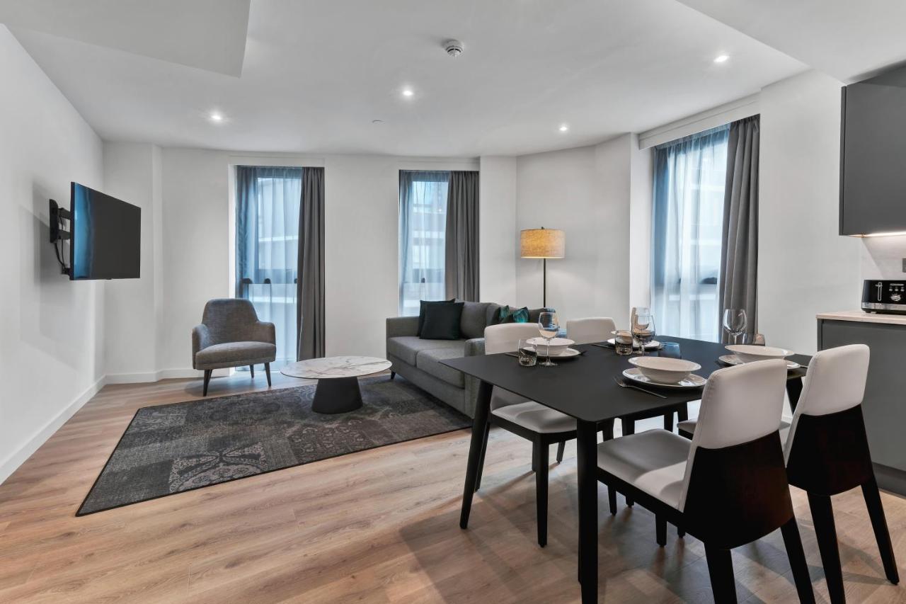 Citysuites 2 Aparthotel Manchester Exteriör bild The photo shows a modern living space that includes a living area and dining area. 

- **Living Area**: There's a gray sofa with a coffee table in front of it, along with a single armchair. A large flat-screen TV is mounted on the wall. The space is 