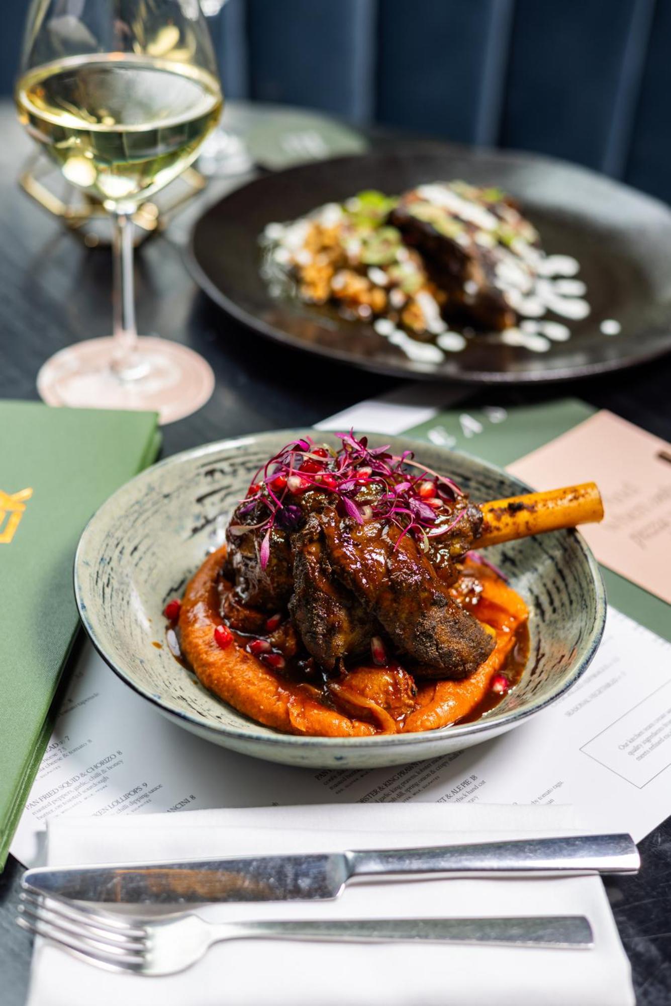 Citysuites 2 Aparthotel Manchester Exteriör bild The photo showcases a beautifully presented dish featuring a piece of slow-cooked meat with a bone, likely lamb, sitting atop a vibrant orange puree. The meat is glazed with a rich sauce and garnished with small pieces of red pomegranate and purple m