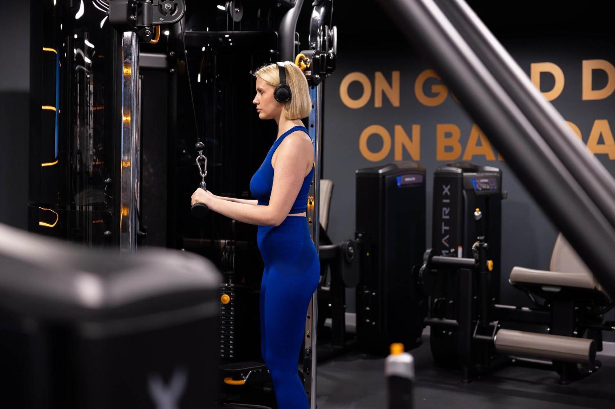 Citysuites 2 Aparthotel Manchester Exteriör bild The photo shows a woman working out in a gym. She is wearing a blue athletic outfit and headphones while using a gym machine. The background features various other gym equipment and a wall with the words "ON GOOD ON BAD" displayed prominently. The se