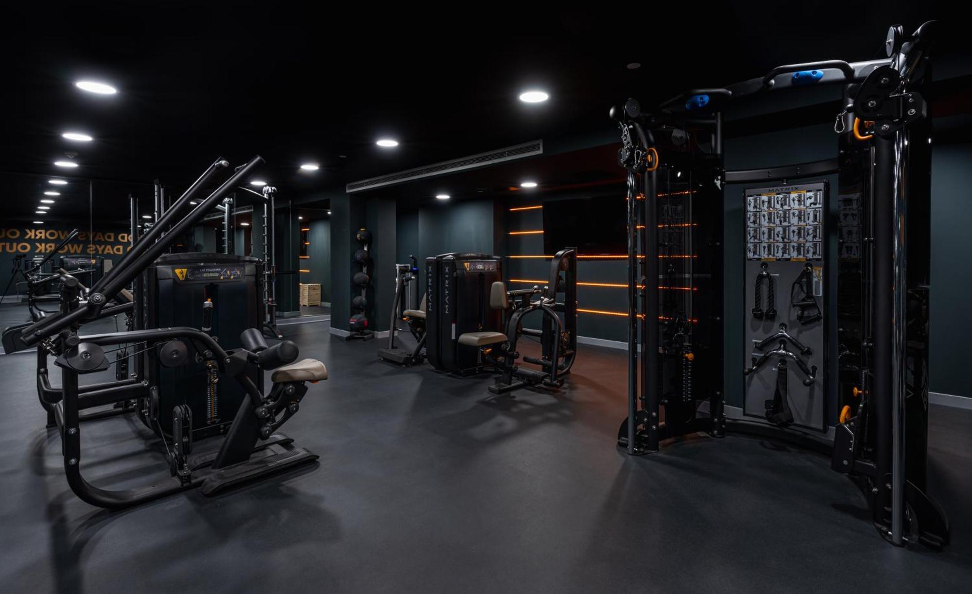 Citysuites 2 Aparthotel Manchester Exteriör bild The photo shows a modern gym or fitness area with various workout machines. The space has a dark color scheme, featuring black walls and flooring. There are multiple pieces of exercise equipment, including stations for strength training, possibly tar