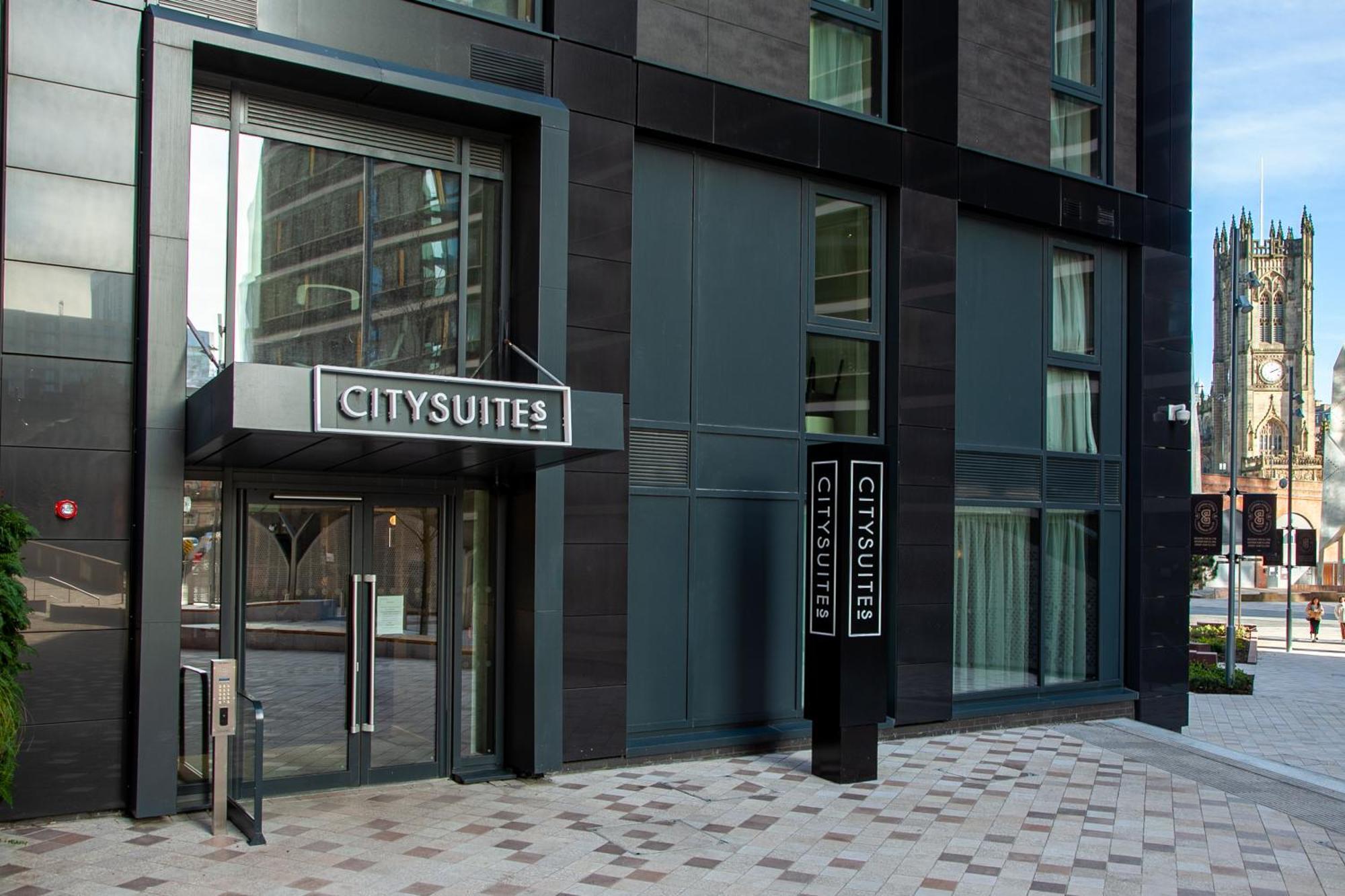 Citysuites 2 Aparthotel Manchester Exteriör bild The photo shows the entrance to a modern building labeled "CITYSUITES." The entrance features large glass doors and a sleek, contemporary design. The building has dark exterior panels and large windows, suggesting a stylish and urban environment. The