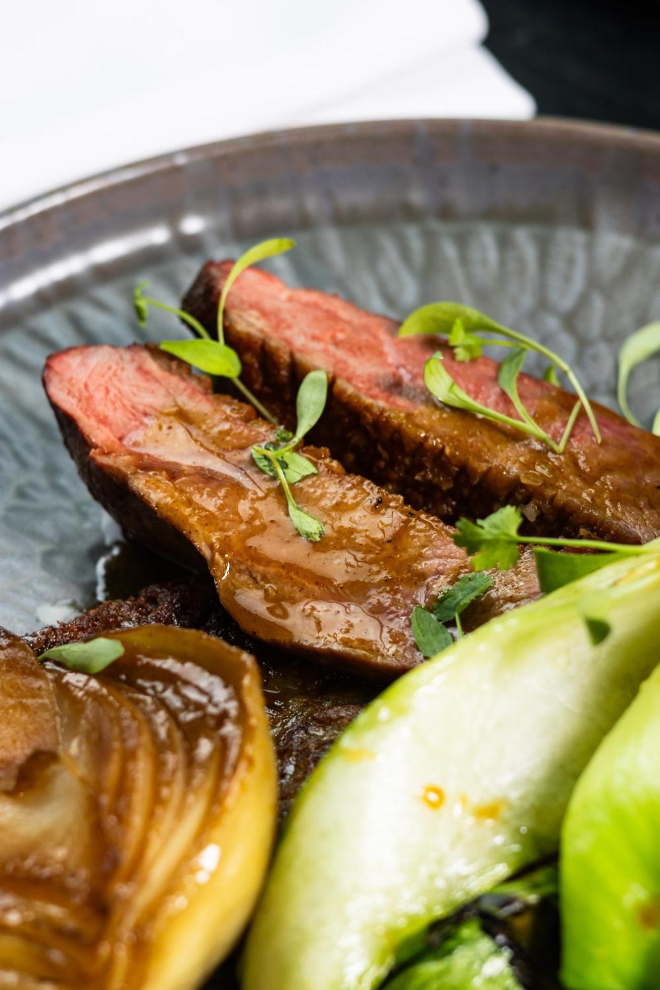 Citysuites 2 Aparthotel Manchester Exteriör bild The photo features slices of meat, likely beef, presented on a decorative plate. The meat appears to have a rich brown sauce drizzled over it and is garnished with fresh herbs, adding a pop of green. There are also some slices of a light-colored vege
