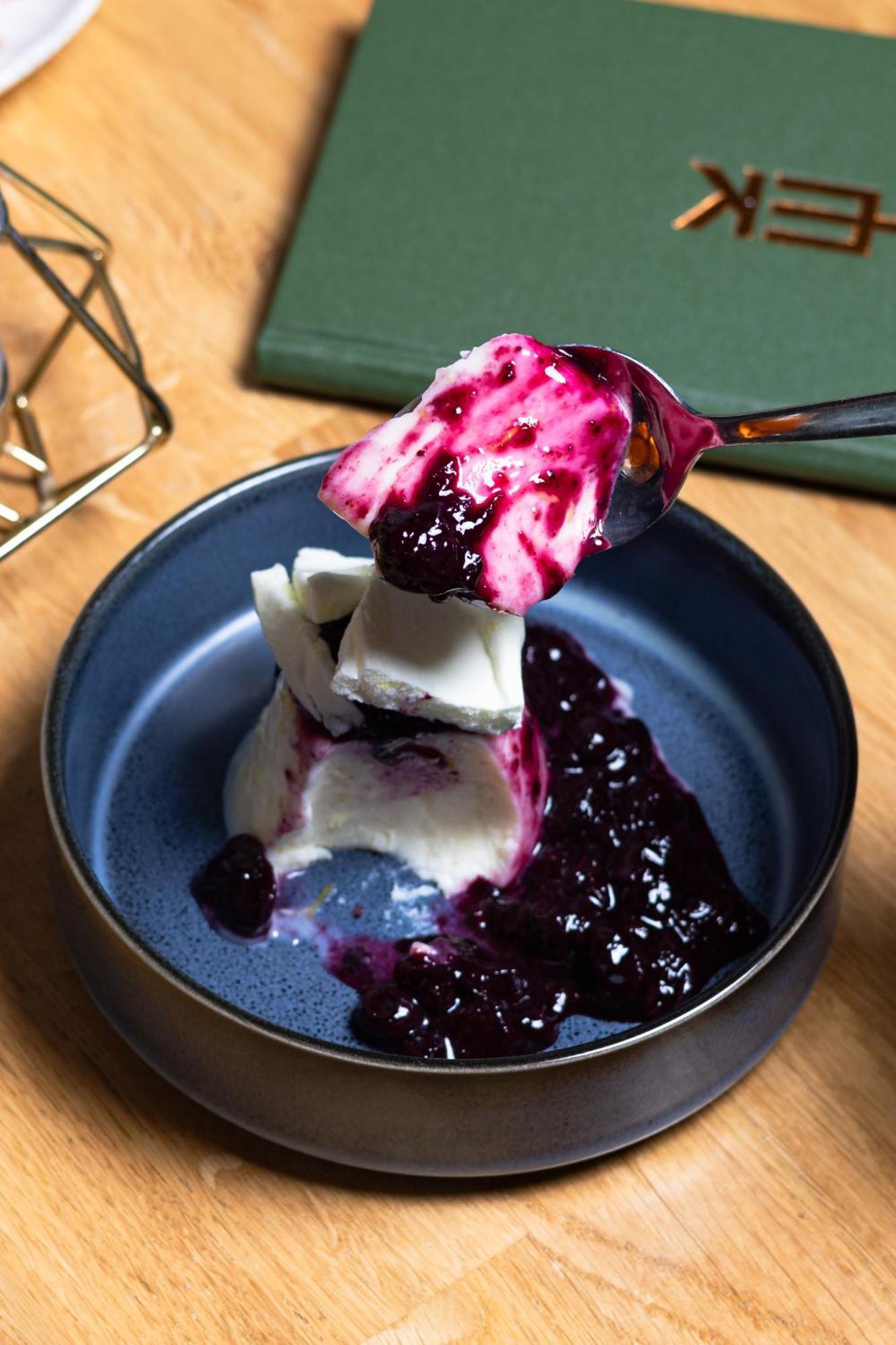 Citysuites 2 Aparthotel Manchester Exteriör bild The photo shows a serving of dessert, likely a type of panna cotta or a creamy custard, partially dished out and accompanied by a rich berry sauce, possibly made from blueberries or blackberries. A spoon with some of the dessert and sauce is hovering